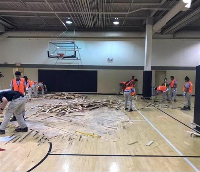 Team members removing damaged flooring in gym.