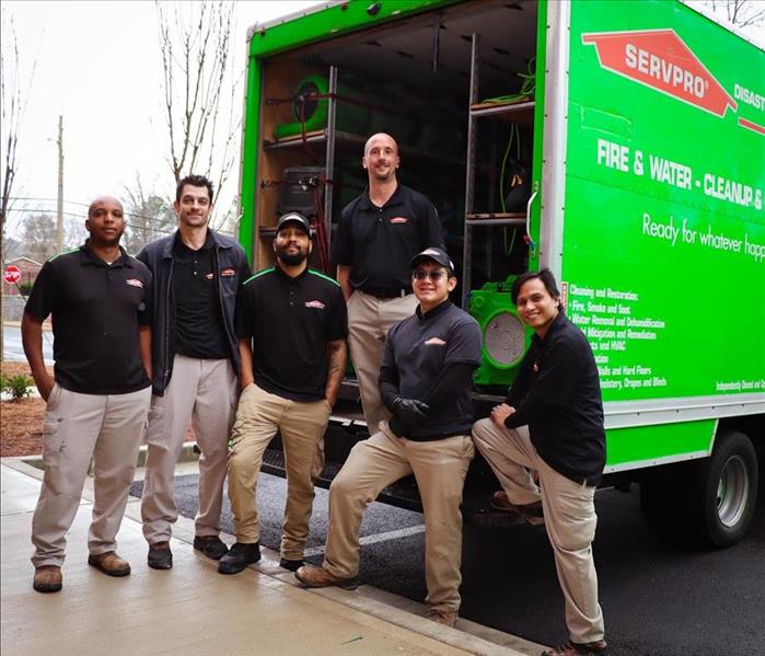 Smiling team of water restoration technicians posing for the camera in front of a green SERVPRO truck with equipment 